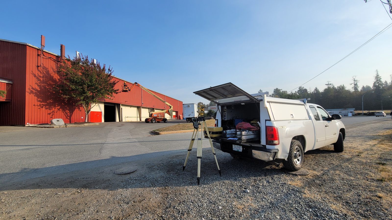 Telecom service truck and tripod-mounted survey instrument at an industrial site